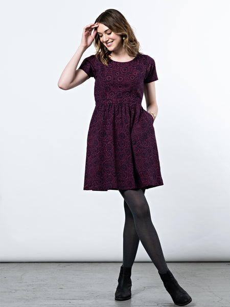 A model wearing the Paper Doll Dress in Magenta with black tights and black booties.