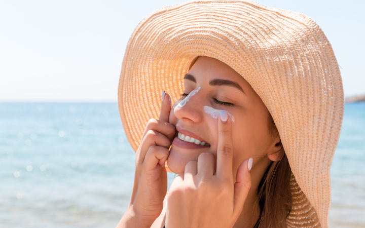 Smiling woman hat applying sunscreen
