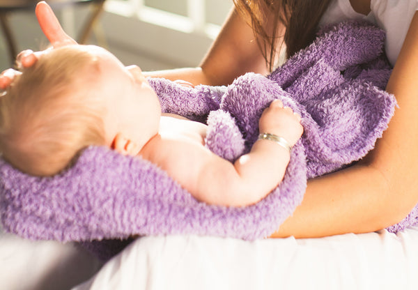 A mother holds her infant in her arms, swaddled in a luxury bamboo Saranoni mini security blanket.
