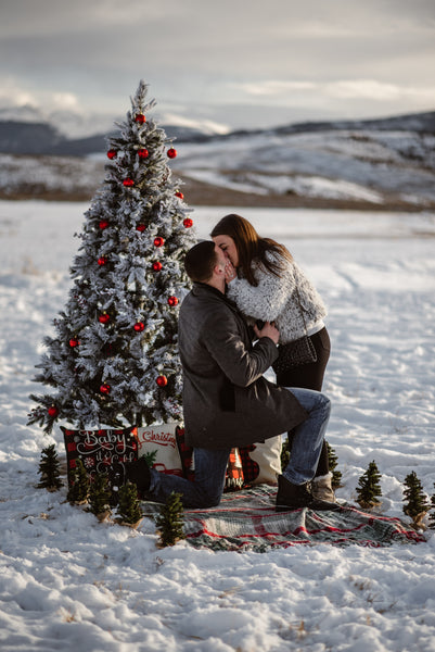 Man proposing in snow with christmas tree 