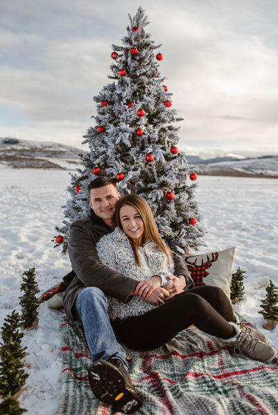 Couple snuggling in snow with christmas tree
