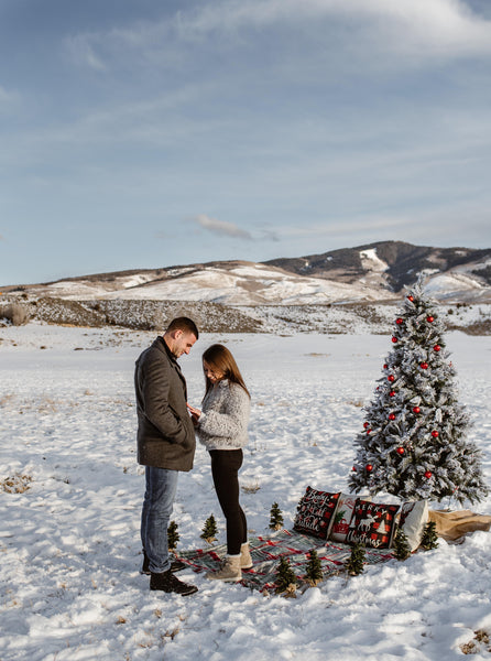 Couple engaged with christmas tree in snow