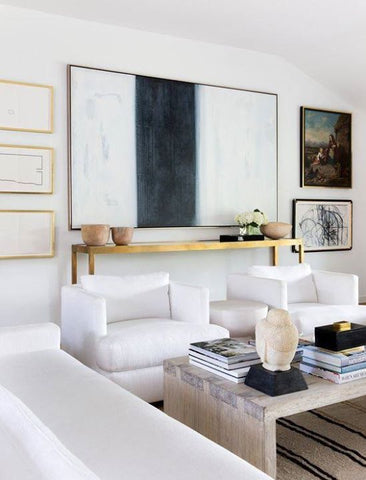 Living room with white sofas and armchairs, large abstract art print and brass furniture and frames