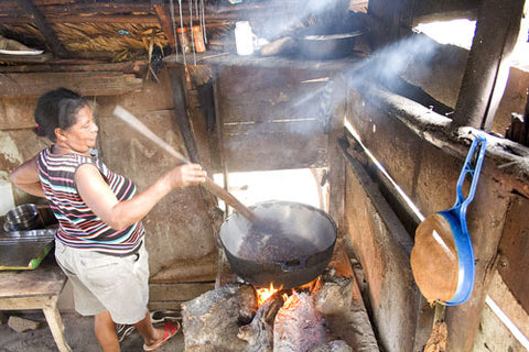Frau in traditioneller Kaffeerösterei röstet Kaffee in einer großen Schüssel über einem offenen Holzfeuer