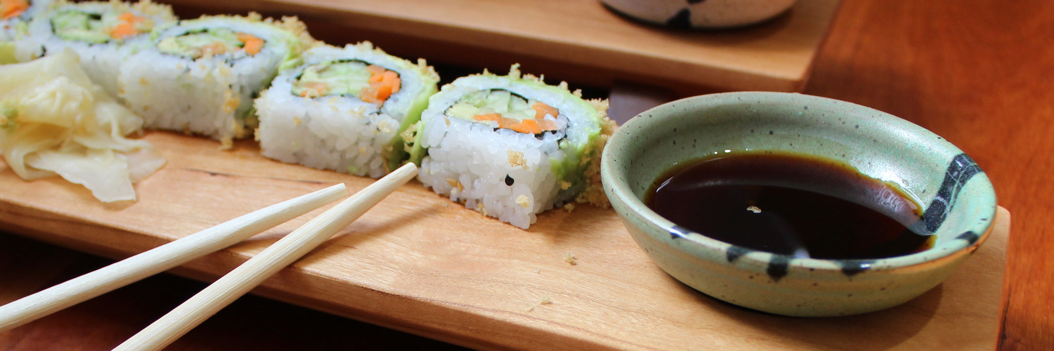 wooden sushi board and a ceramic dipping bowl with sushi and chopsticks