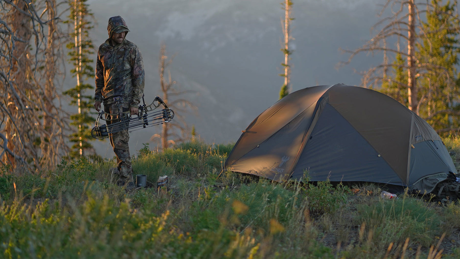 Man wearing camo holding bow next to tent