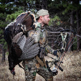 man wearing hunting accessories carrying bow and turkey