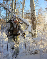 man with snow camo accessories hiking through snowy forest