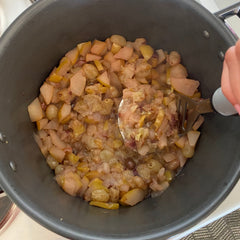cooked pears and grapes in a pot being mashed by hand to make jam