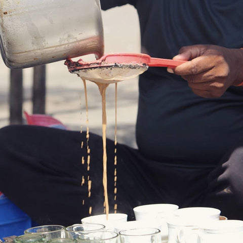 chai being strained through a strainer into lots of white teacups