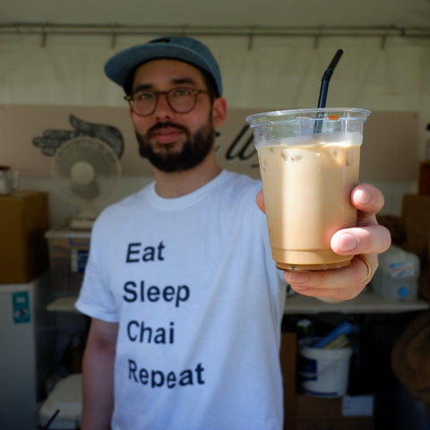 Man in white tshirt holding plastic cup with iced chai in it