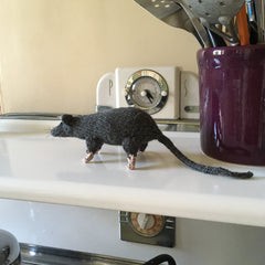 a knitted rat stands on the top of an old stove