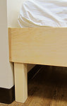 Corner of an unfinished maple platform bed, with a mattress on it