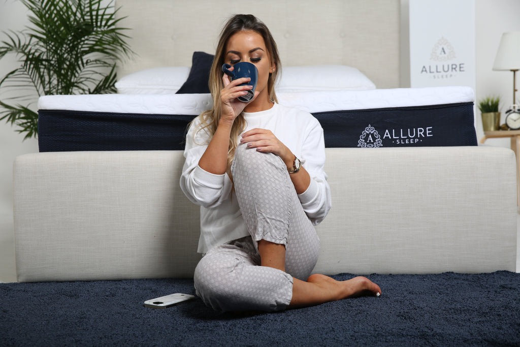 Woman sitting beside mattress drinking from a mug