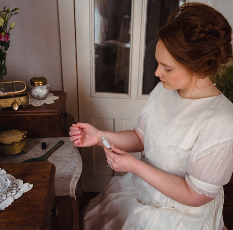 Victorian woman applying perfume oil at antique vanity