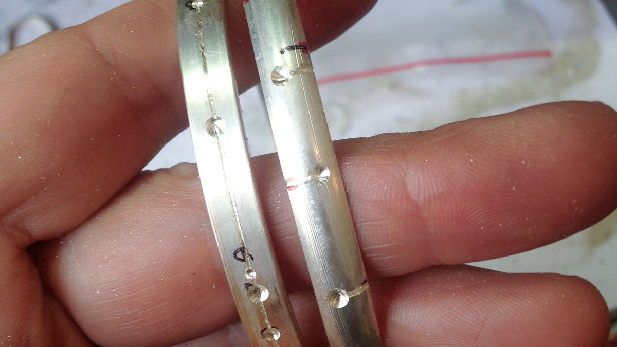 A hand holding two almost completed bangles.