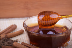 A bowl of amber coloured honey with a honey dipper on a table with cinnamon sticks