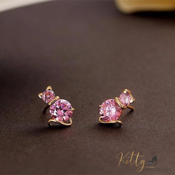 golden cat earrings with pink amethysts lying on black surace