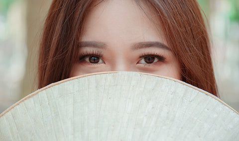 woman with fan covering the face and eye exposed