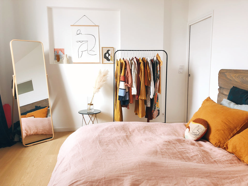 bedroom with mirror, clothes rack and orange pillows
