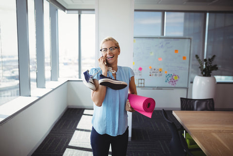 Female executive holds exercise mat and shoes in the office