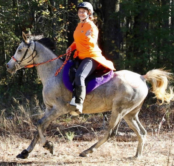 A woman riding a grey horse wearing Scoot Boots in a horse riding competition 