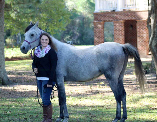 Woman posing with her grey horse on the grass