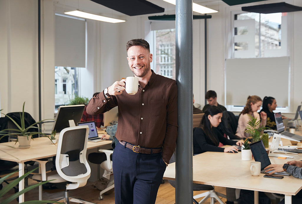 Lee leaning against a post in his office drinking a cup of coffee