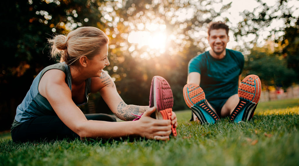 Nainen ja mies venyttelevät ulkona nurmikon päällä. Superdieetti® ja VHH-valmennukset tuovat elämääsi energiaa!