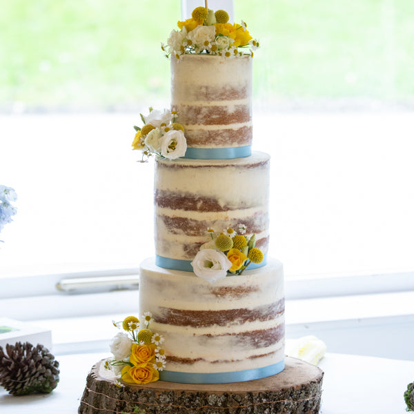 Joanne and Ross' semi naked wedding cake with white and yellow flowers