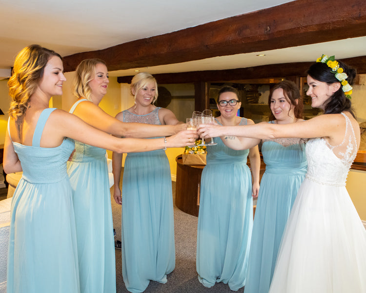 Bridesmaids in duck egg blue dresses all holding prosecco and the bride on the right