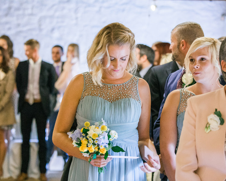 Bridesmaid Alice in a duck egg blue dress looking at her reading with a bouquet in her hand