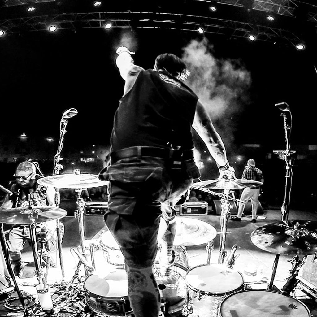 Black & white photo of Brandon Steineckert climbing on his drums during a concert.