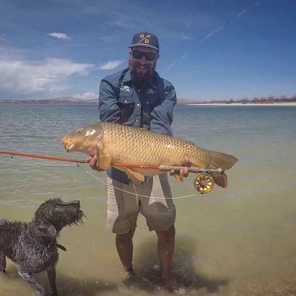 Colby Crossland holding a large fish with his dog Forelle in the water next to him.
