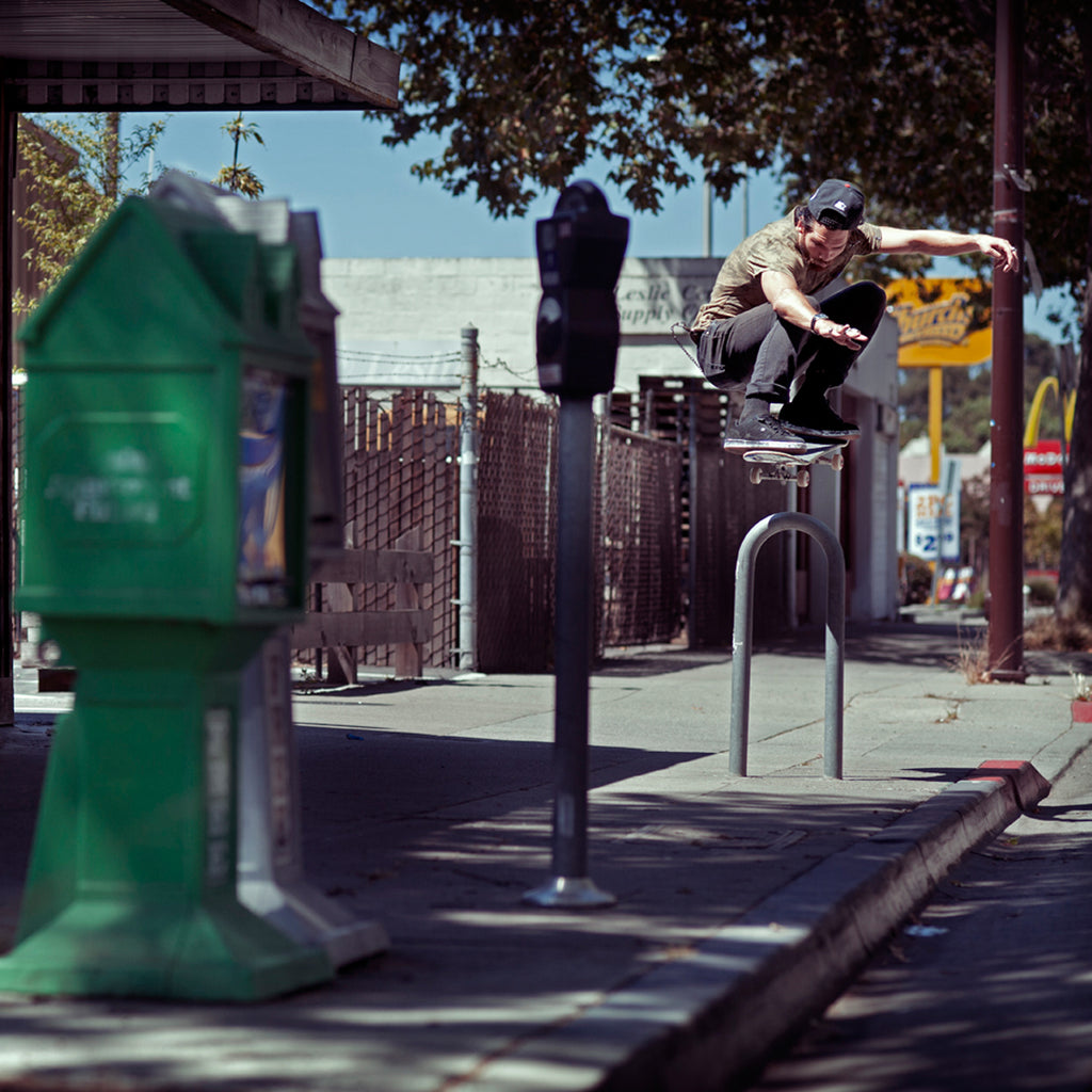 Corey Duffel doing an ollie on his skateboard over a bike rack on the sidewalk.