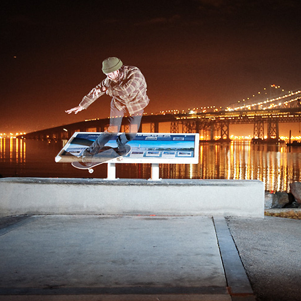 Corey Duffel doing a backside smith grind on his skateboard in front of the Bay Bridge.