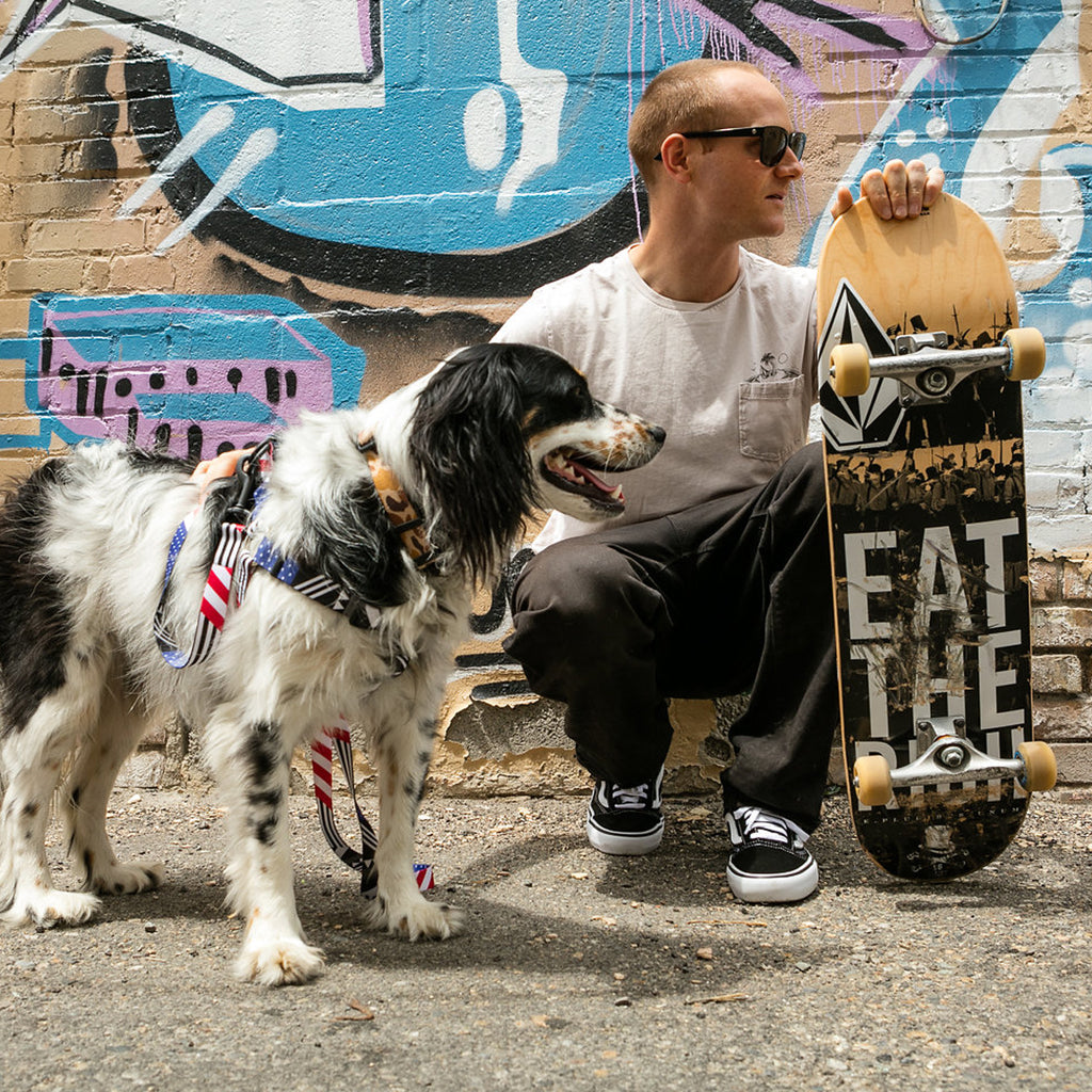 Pat Moore crouching down holding his skateboard with his dog Murphy.