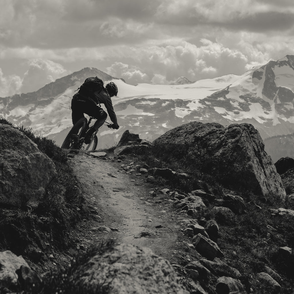 Eric Porter riding his mountain bike on a rocky trail with snowy mountains in the background.