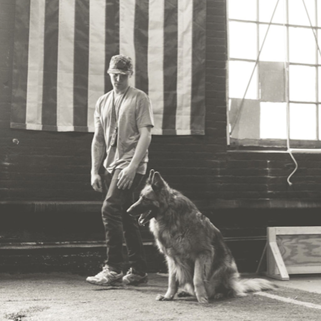 Black & white photo of Thomas Davis working with a German Shepard in front of an American flag.