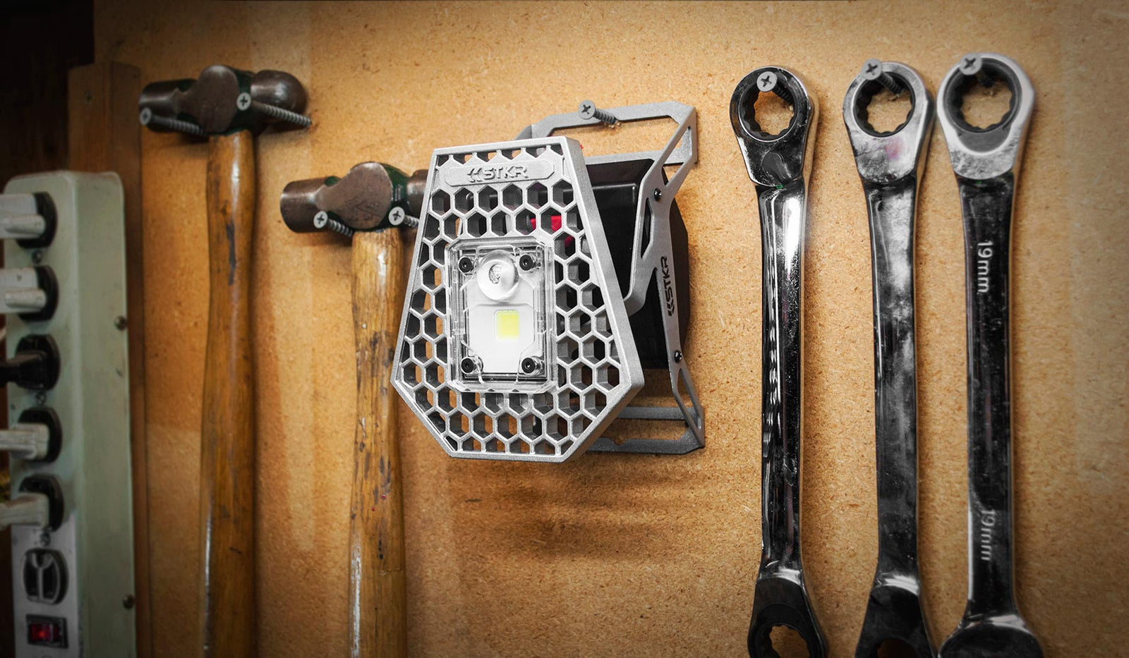 The Mobile Task Light hanging on a garage tool wall next to a couple hammers and a couple box end wrenches