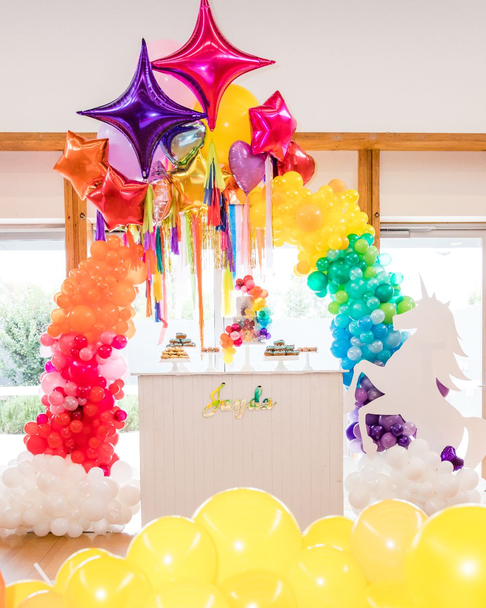 Dessert table with intricate handmade desserts, unicorn cake, rainbow balloon arch and unicorn.