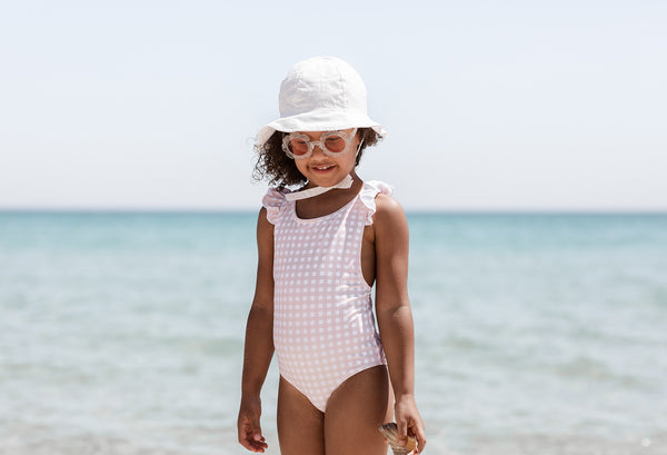 Girl on beach wearing Willow Swim childrens swimsuit hat and sunglasses