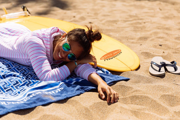 girl laying with surfboard on beach in sand