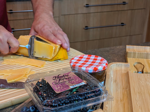 Cutting gouda for cheese board with fruits and jam in foreground