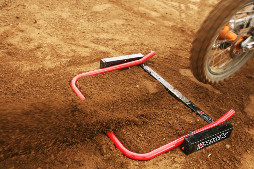 Extreme close up of a Risk Racing Holeshot race gate that has dropped and a spinning back tire leaving screen right.