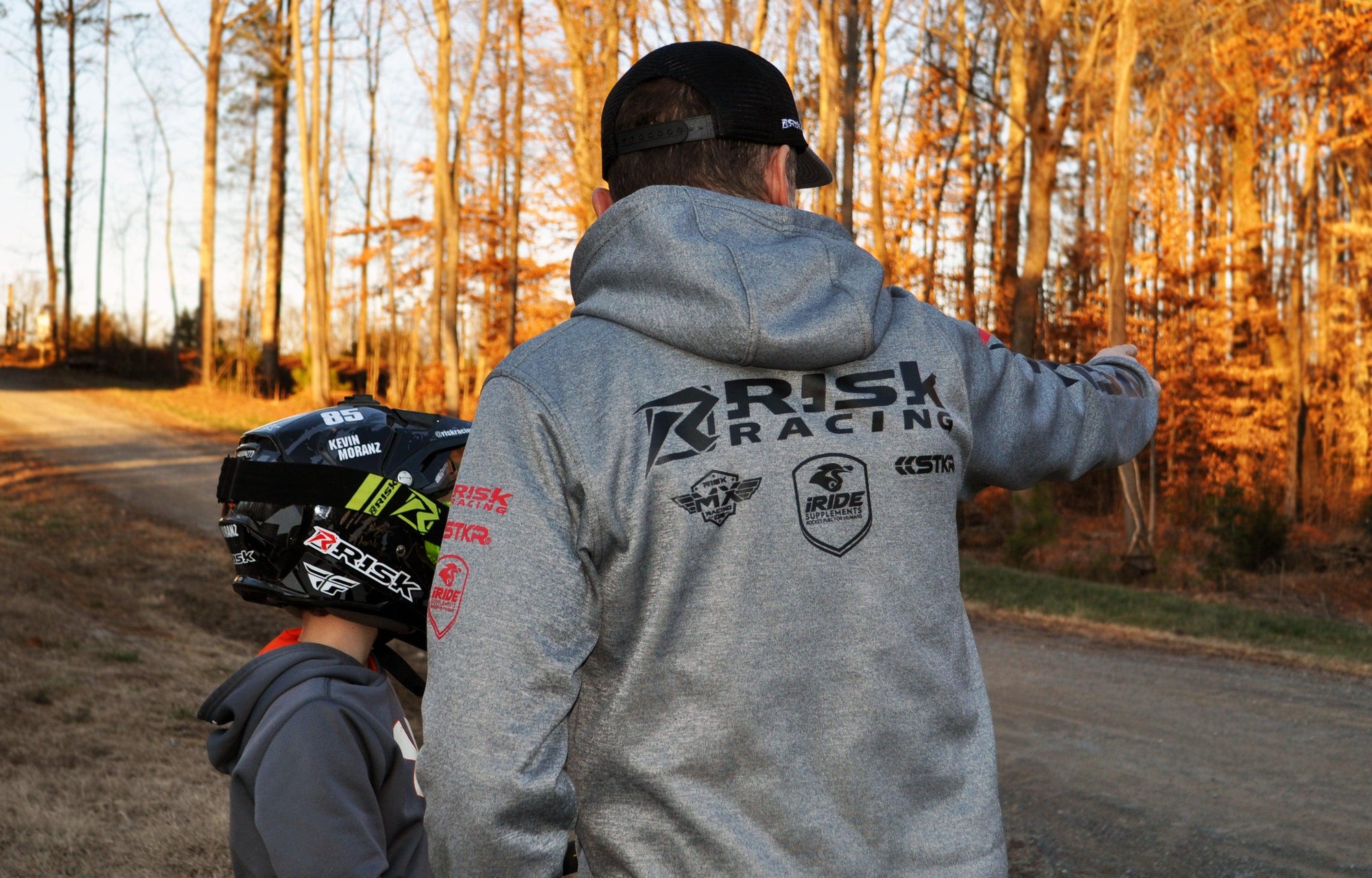 Male wearing the new Risk Zipper hoodie standing next to a young man wearing a black MX helmet. captured from behind showing the back of the jacket.