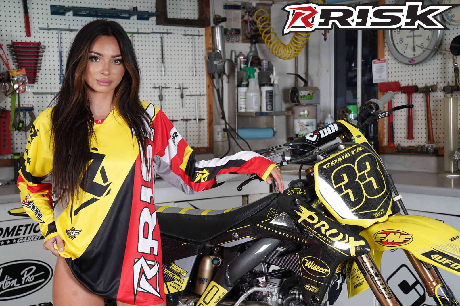 August's Risk Racing Moto Model Samantha Heady posing in various bikinis & Risk Racing Jerseys next to a dirt bike that's sitting on a Risk Racing ATS stand - Pose #24