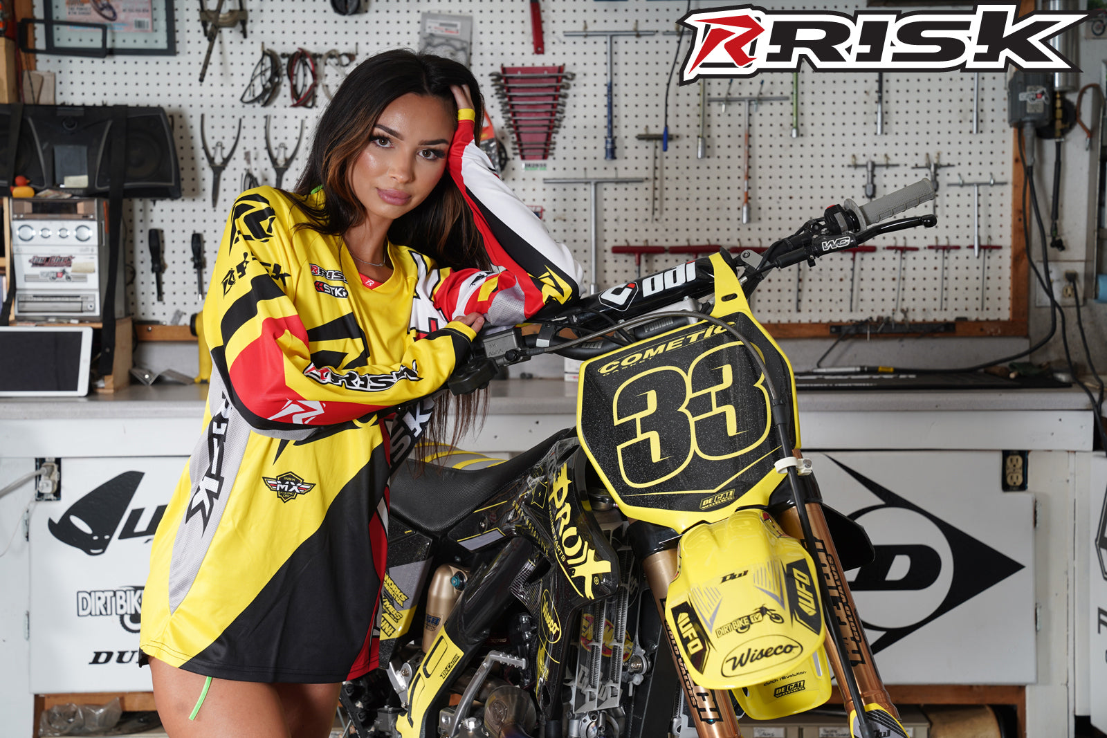 August's Risk Racing Moto Model Samantha Heady posing in various bikinis & Risk Racing Jerseys next to a dirt bike that's sitting on a Risk Racing ATS stand - Pose #26