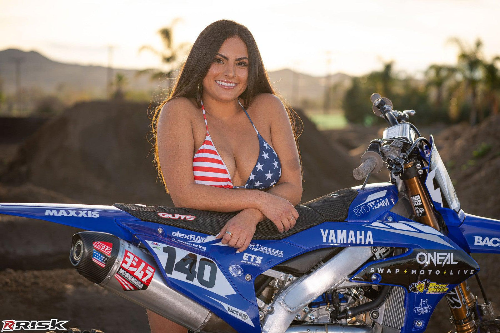 December's Risk Racing Moto Model Kelly Perez posing in various bikinis and Risk Racing Jerseys next to a dirt bike that's sitting on a Risk Racing ATS stand - Pose #11