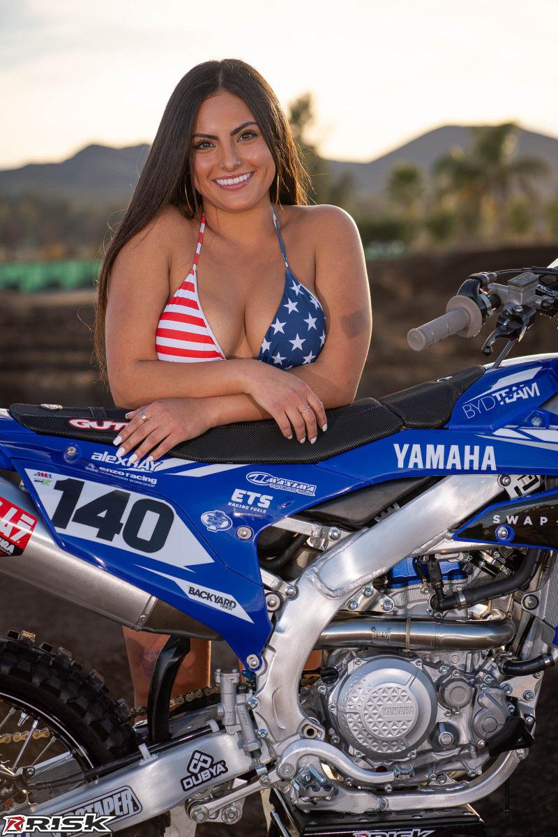 December's Risk Racing Moto Model Kelly Perez posing in various bikinis and Risk Racing Jerseys next to a dirt bike that's sitting on a Risk Racing ATS stand - Pose #9